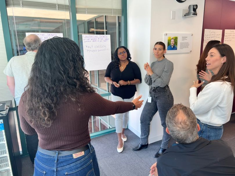 Udemy employees stand discussing ideas near a wall with their meeting notes.&nbsp;