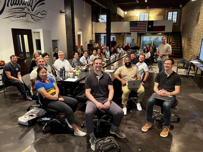 A group of employees sitting in chairs and smiling at the camera.