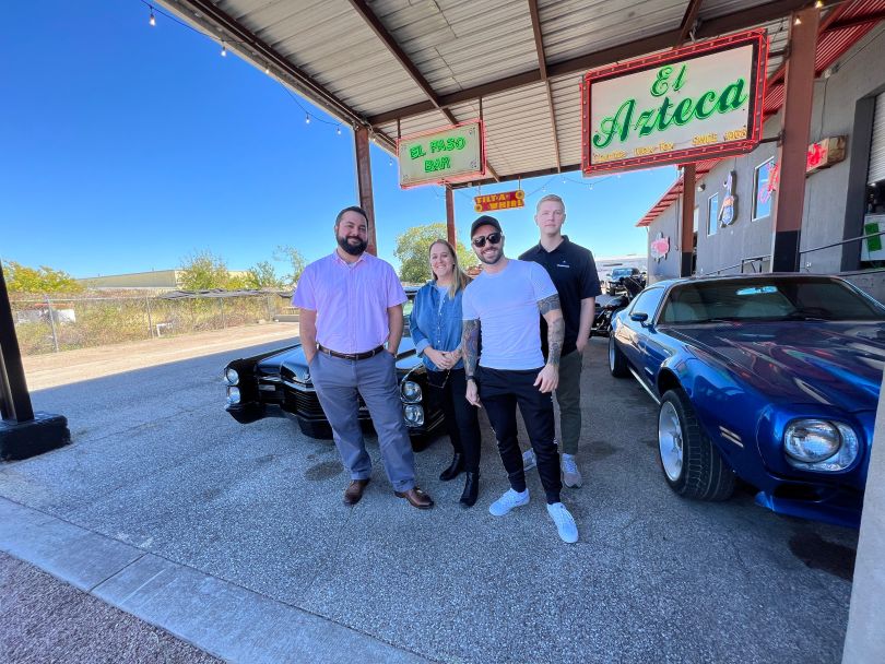 four employees outside El Paso Bar with cars 